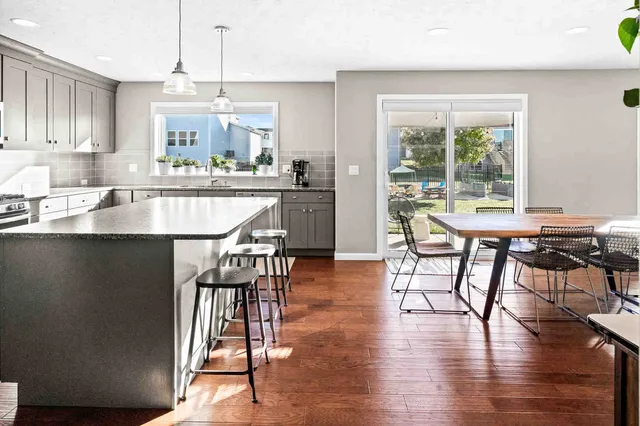 a kitchen with stainless steel appliances granite countertop a stove top oven a sink a dining table and chairs with wooden floor