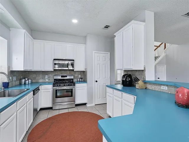 a kitchen with stainless steel appliances a stove a sink a refrigerator white cabinets and wooden floor