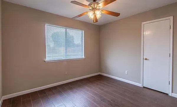 an empty room with wooden floor chandelier fan and windows