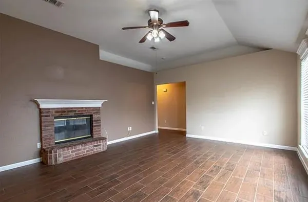 a view of an empty room with wooden floor fireplace and a window