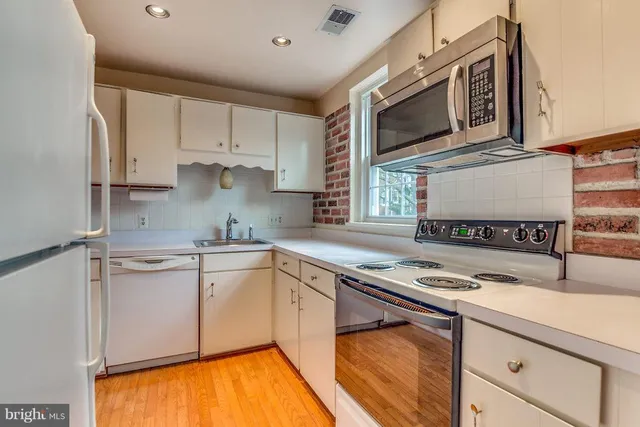 a kitchen with stainless steel appliances granite countertop a stove top oven a sink dishwasher and white cabinets with wooden floor