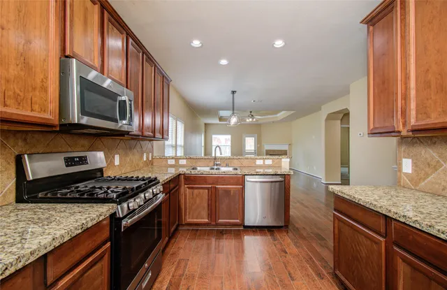 a kitchen with stainless steel appliances granite countertop wooden cabinets a stove a sink and a microwave