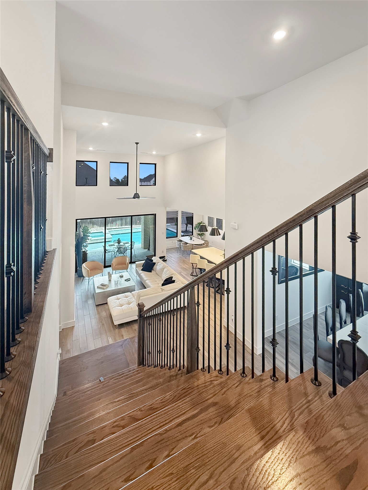 26918 Swanborough Road Spring, TX 77389 - Photo 50 of 50 Looking down from the second-floor loft, the wrought-iron staircase frames a sweeping view of the two-story living room, dining area, and backyard pool beyond — a perspective that captures the full scale of this open floor plan.