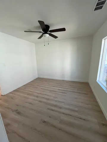 an empty room with wooden floor fan and windows
