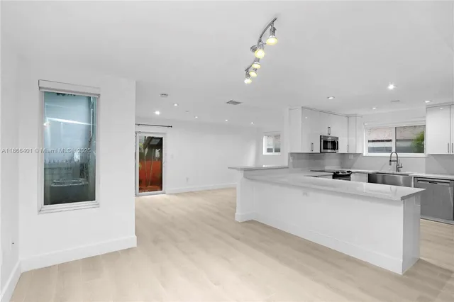 a large white kitchen with kitchen island a sink a stove a refrigerator and a dining table