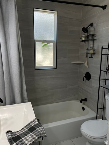 857 27th Street Ogden, UT 84403 - Photo 6 of 20 Bathroom featuring light gray tiled shower surround, a white bathtub, black fixtures, and a rectangular frosted window