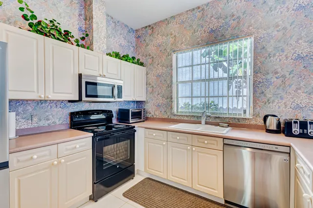 a kitchen with stainless steel appliances granite countertop white cabinets a sink a stove a microwave and a window