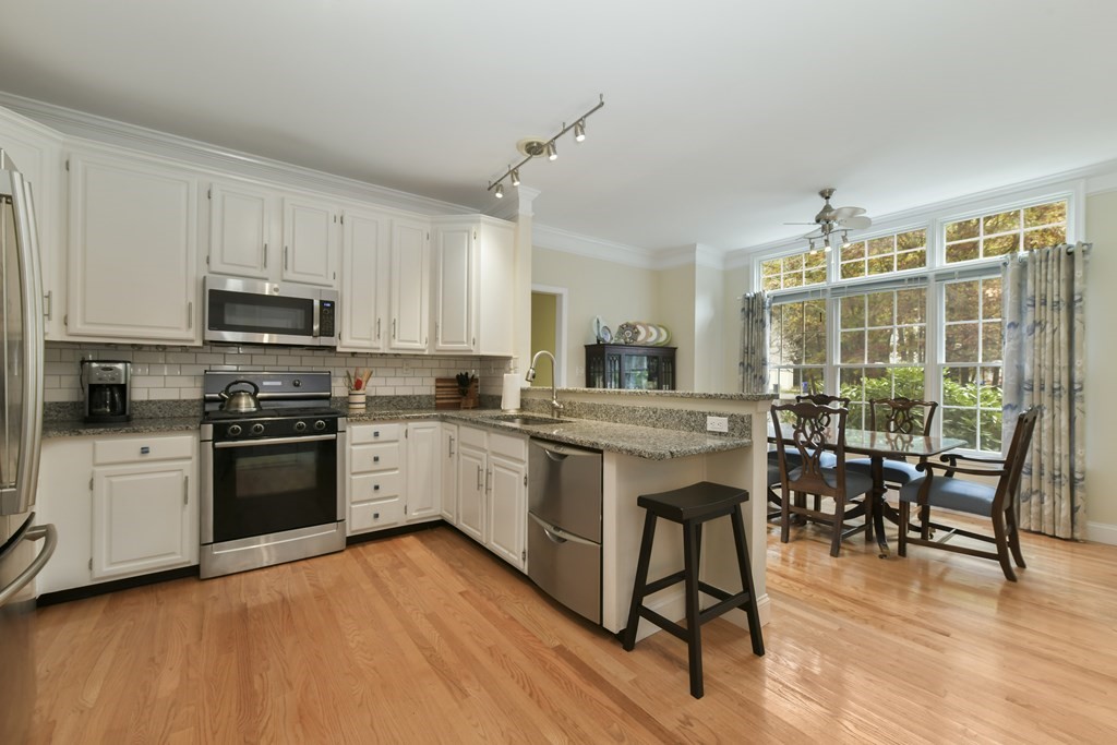 7 Moore Circle, Unit 7 Bedford, MA 01730 - Photo 9 of 27 a kitchen with stainless steel appliances kitchen island granite countertop a stove top oven a sink a dining table and chairs