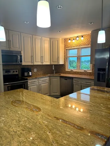 a large kitchen with stainless steel appliances a large counter top a stove a sink dishwasher and a flat tv screen