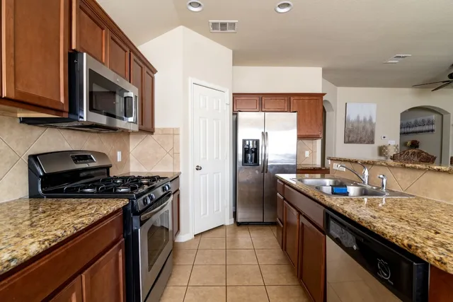 a kitchen with stainless steel appliances granite countertop a stove top oven a sink a refrigerator and a microwave