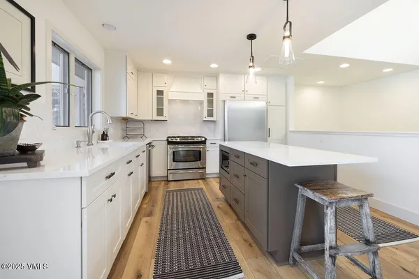 a large white kitchen with a stove a sink dishwasher and a refrigerator with wooden floor