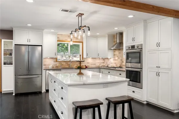 a kitchen with stainless steel appliances granite countertop a refrigerator a sink dishwasher a stove and white cabinets with wooden floor