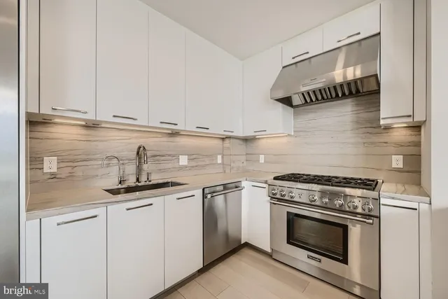 a open kitchen with granite countertop a stove a sink and white cabinets with wooden floor