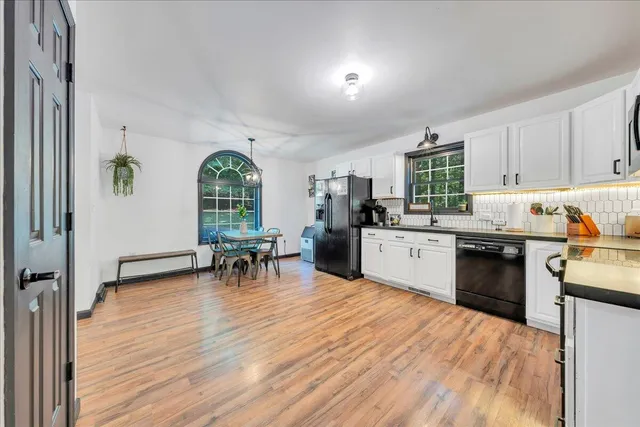 a kitchen with stainless steel appliances granite countertop a stove top oven a sink a dining table and chairs with wooden floor