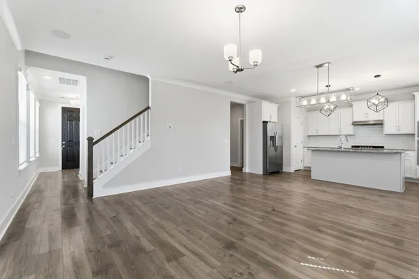 a view of an empty room and kitchen with wooden floor