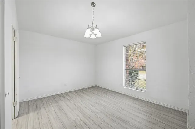 an empty room with wooden floor chandelier and windows