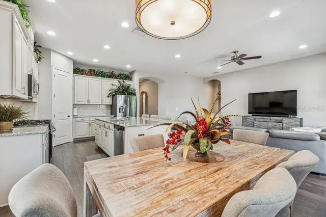 a kitchen with stainless steel appliances granite countertop a sink a stove a refrigerator cabinets and a dining table with wooden floor