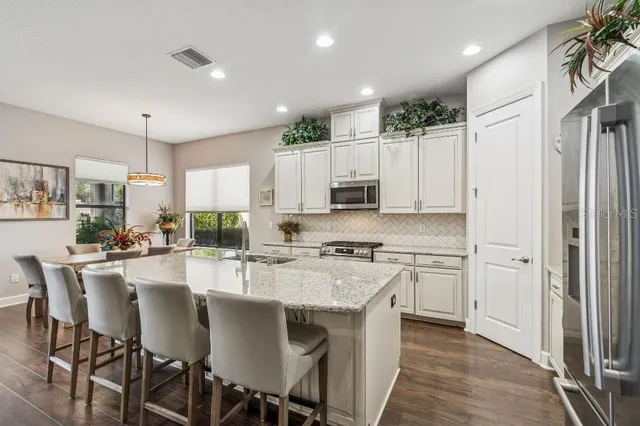 a kitchen with stainless steel appliances granite countertop a stove top oven a refrigerator a sink and white cabinets with wooden floor