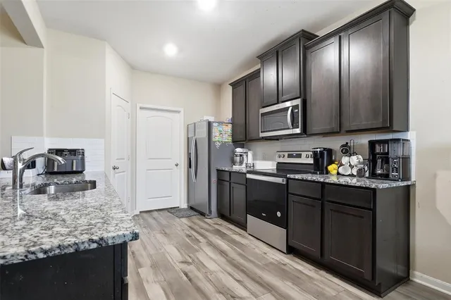 a kitchen with stainless steel appliances kitchen island granite countertop a dining table chairs and a refrigerator