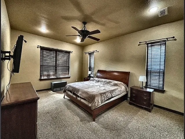 a spacious bedroom with a bed a dresser and a flat screen tv