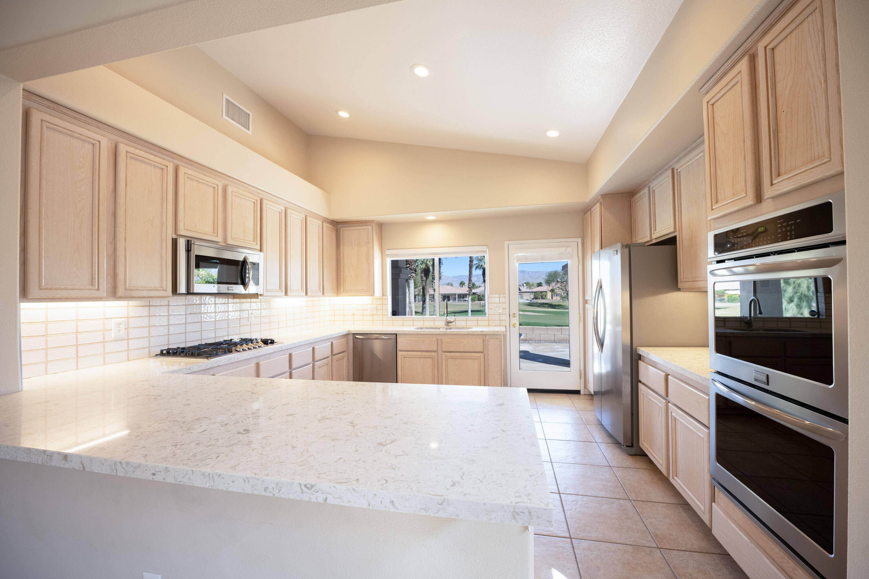 80162 Pebble Beach Drive Indio, CA 92201 - Photo 11 of 48 a large kitchen with stainless steel appliances granite countertop a large stove top oven a sink dishwasher and white cabinets with wooden floor