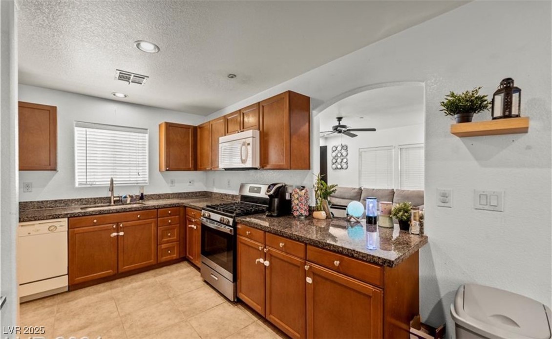 7708 Custom Weave Court Las Vegas, NV 89149 - Photo 7 of 32 Kitchen with white appliances, brown cabinetry, a textured ceiling, a ceiling fan, and dark stone counters