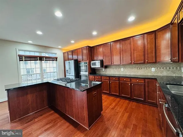 a kitchen with stainless steel appliances granite countertop wooden cabinets a stove a sink and dishwasher with wooden floor