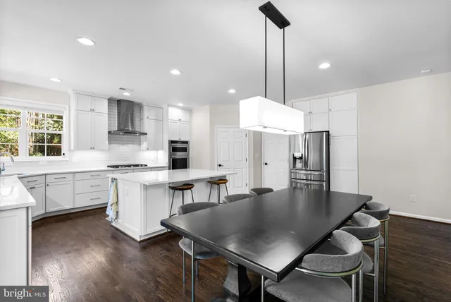 a kitchen with stainless steel appliances granite countertop a table chairs a sink dishwasher a stove and a dining table with wooden floor