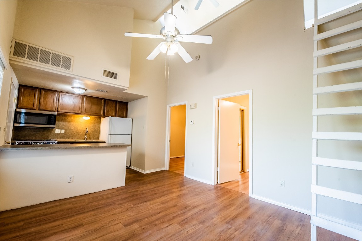 601 Nelray Boulevard, Unit 5 Austin, TX 78751 - Photo 3 of 13 Kitchen with brown cabinets, light wood-style flooring, a towering ceiling, tasteful backsplash, and stainless steel microwave