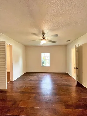 an empty room with wooden floor chandelier fan and windows