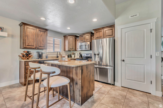 1071 Jamie-Matt Circle Layton, UT 84041 - Photo 23 of 28 Kitchen with stainless steel appliances, light stone counters, a center island, wood finish cabinetry, and a breakfast bar