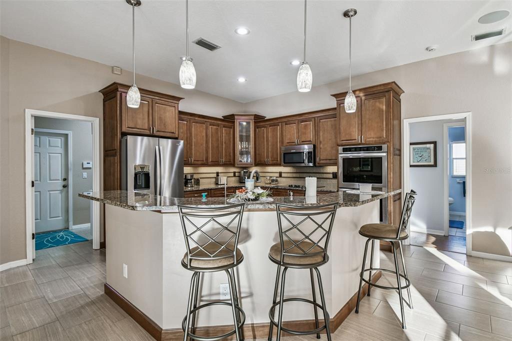 1955 Dunloe Circle Dunedin, FL 34698 - Photo 21 of 94 a kitchen with stainless steel appliances kitchen island granite countertop a refrigerator a stove a oven a sink with island chairs and wooden cabinets
