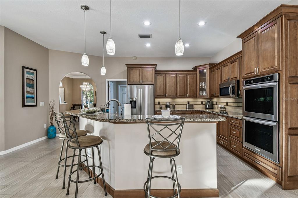 1955 Dunloe Circle Dunedin, FL 34698 - Photo 22 of 94 a kitchen with stainless steel appliances kitchen island granite countertop a stove top oven a refrigerator a sink and chairs with wooden floor