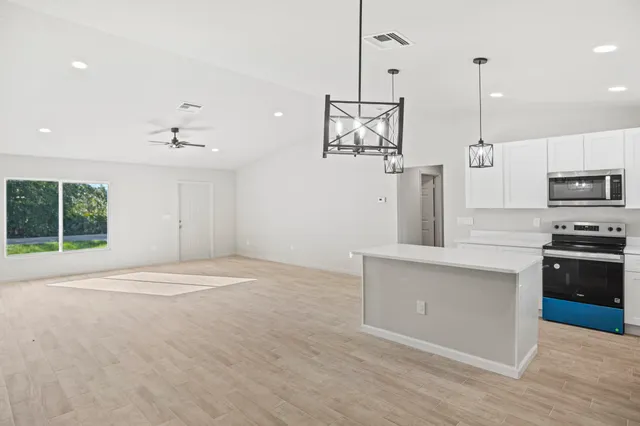 a kitchen with stainless steel appliances granite countertop a sink a stove a refrigerator and white cabinets with wooden floor