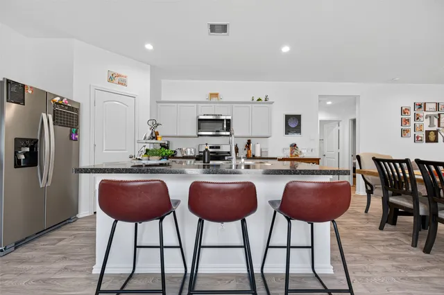 a kitchen with stainless steel appliances granite countertop a dining table chairs refrigerator and sink