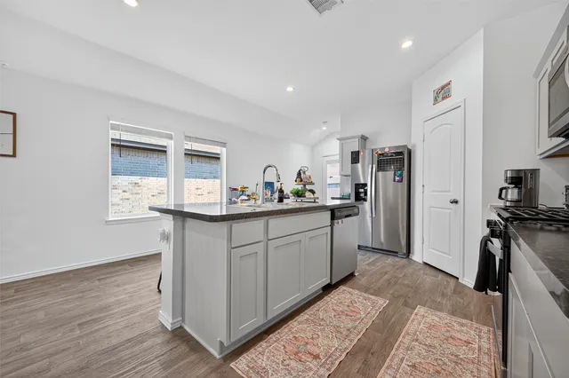 a kitchen with stainless steel appliances granite countertop a refrigerator a stove and a sink with wooden floor