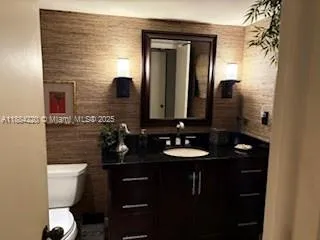 a bathroom with a toilet sink vanity granite and shower