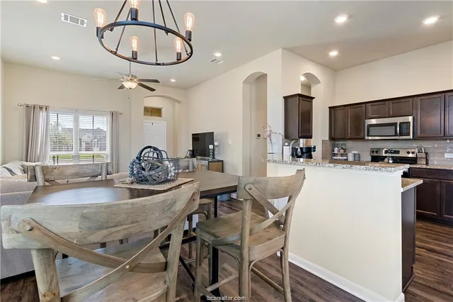 a kitchen with stainless steel appliances granite countertop a dining table chairs refrigerator and microwave
