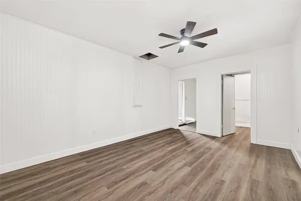 a view of an empty room with wooden floor and a ceiling fan