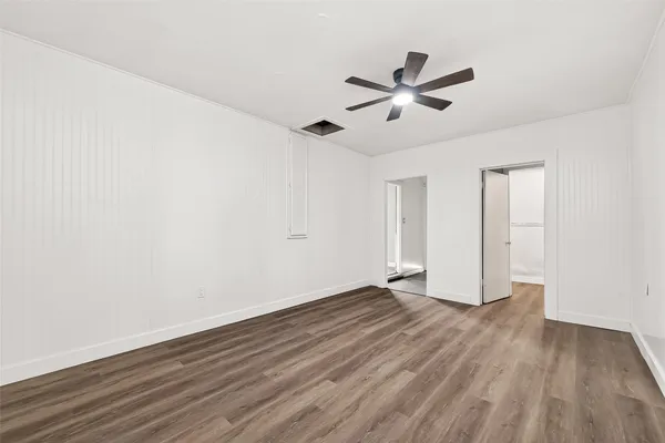 a view of an empty room with wooden floor and a ceiling fan