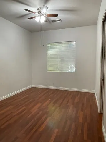 an empty room with wooden floor chandelier fan and windows