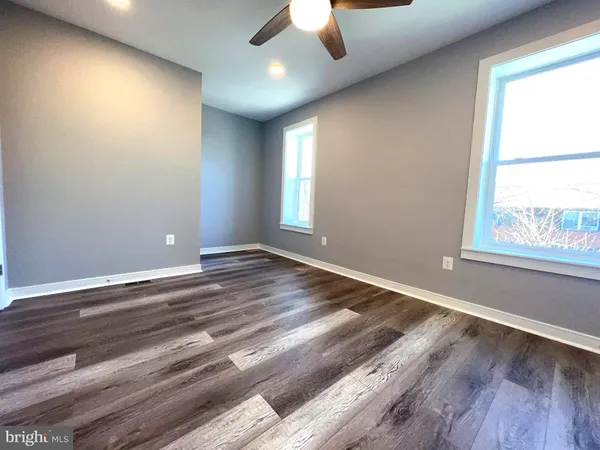 an empty room with wooden floor fan and windows