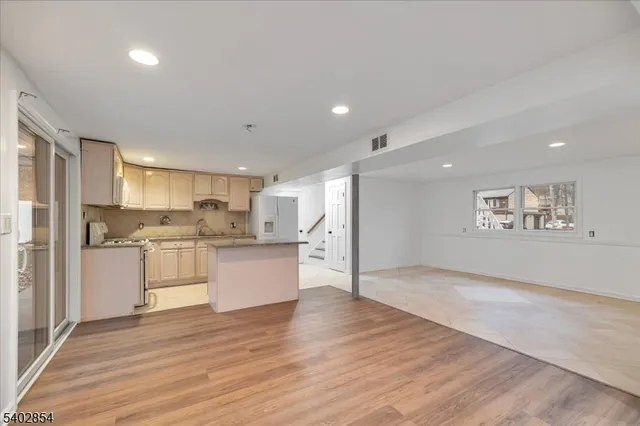 a large kitchen with kitchen island a refrigerator a sink dishwasher a stove and white cabinets with wooden floor