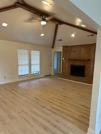 an empty room with wooden floor fireplace and windows