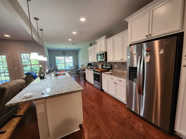 a kitchen with stainless steel appliances granite countertop a refrigerator a sink dishwasher a stove and white countertops with wooden floor