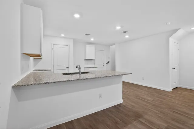 a large kitchen with granite countertop a sink and white cabinets with wooden floor