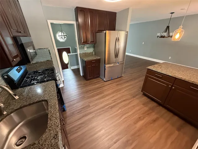 a kitchen with stainless steel appliances granite countertop a refrigerator a stove and a wooden floors