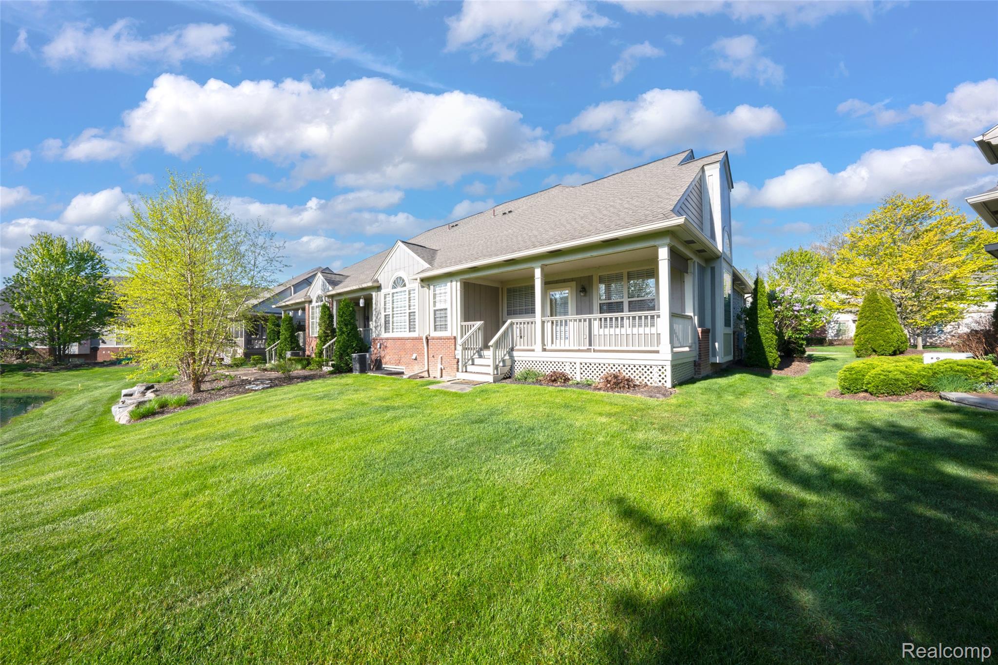 3805 Windingbrook Circle, Unit 22 Rochester, MI 48309 - Photo 62 of 63 Expansive green lawn surrounds the property, featuring a covered porch with white railings, a brick foundation accent, and mature trees