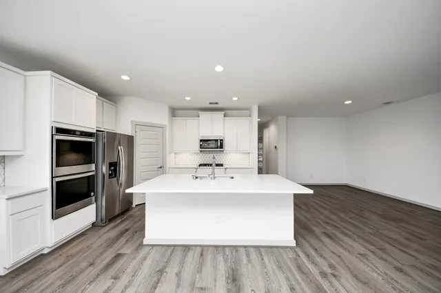 a large white kitchen with wooden floor and stainless steel appliances