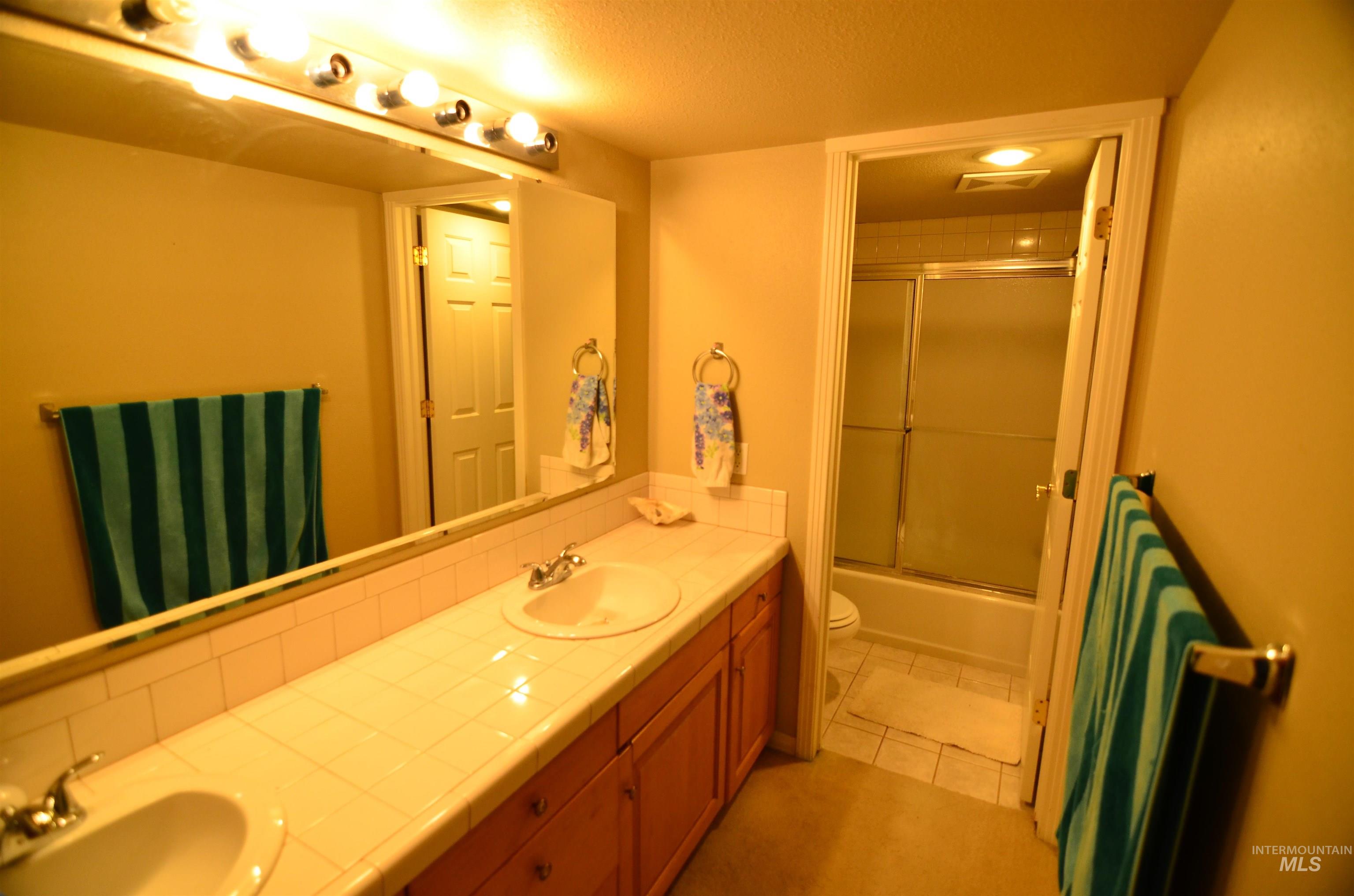 690 Granite Way Boise, ID 83712 - Photo 13 of 30 Full bathroom with combined bath / shower with glass door, a textured ceiling, double vanity, and light tile patterned floors